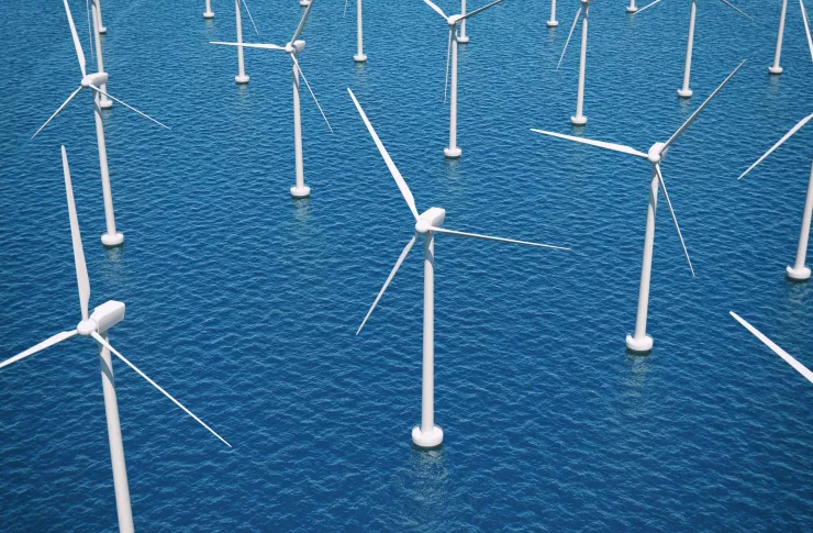 Aerial view of an offshore wind farm with white turbines standing in blue open water.